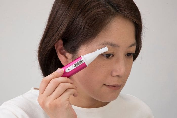 女性はピンクの電動歯ブラシを使って顔をきれいにしています。