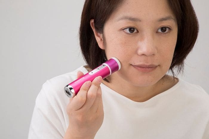 女性はピンクの電動歯ブラシを使って顔をきれいにしています。