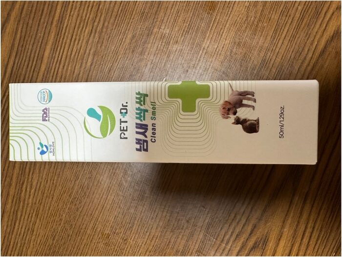 ペットドクター クリーン スメル (クリーンスメル) の白い箱、ペット消臭用、50 ml/1.29 オンス。猫と犬の画像、緑の医療十字、ロゴが木の表面に表示されています。.