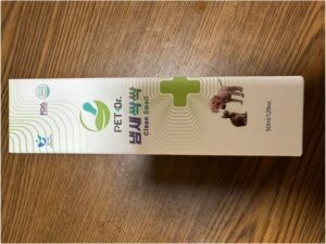ペットドクター クリーン スメル (クリーンスメル) の白い箱、ペット消臭用、50 ml/1.29 オンス。猫と犬の画像、緑の医療十字、ロゴが木の表面に表示されています。.