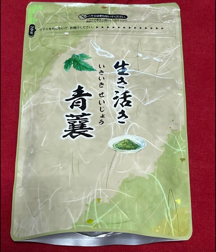 ベージュと緑の再封可能な食品パッケージ。赤い表面に、「生き活き青襄」という日本語の文字と、小さな皿に刻んだ緑のハーブが載った画像が描かれています。.