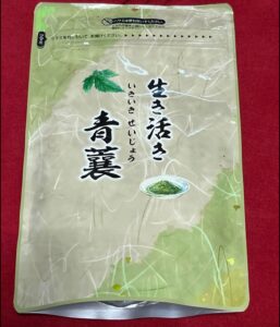 ベージュと緑の再封可能な食品パッケージ。赤い表面に、「生き活き青襄」という日本語の文字と、小さな皿に刻んだ緑のハーブが載った画像が描かれています。.