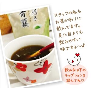 花柄のソーサーに、赤いスプーンと紅茶のカップが置かれています。その後ろには「生き活き青襄」と書かれた緑茶のパッケージがあります。側面には日本語の文字と、ハートと吹き出しが付いた鶏のイラストが描かれています。.