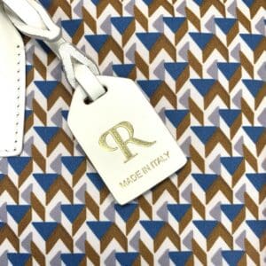 ゴールドの「R」の文字と「MADE IN ITALY」の文字が入った白いレザータグのアップ。このディテールが、ROBERTA PIERI TATAMI スモールトートのイタリアン・クラフツマンシップを際立たせている。.