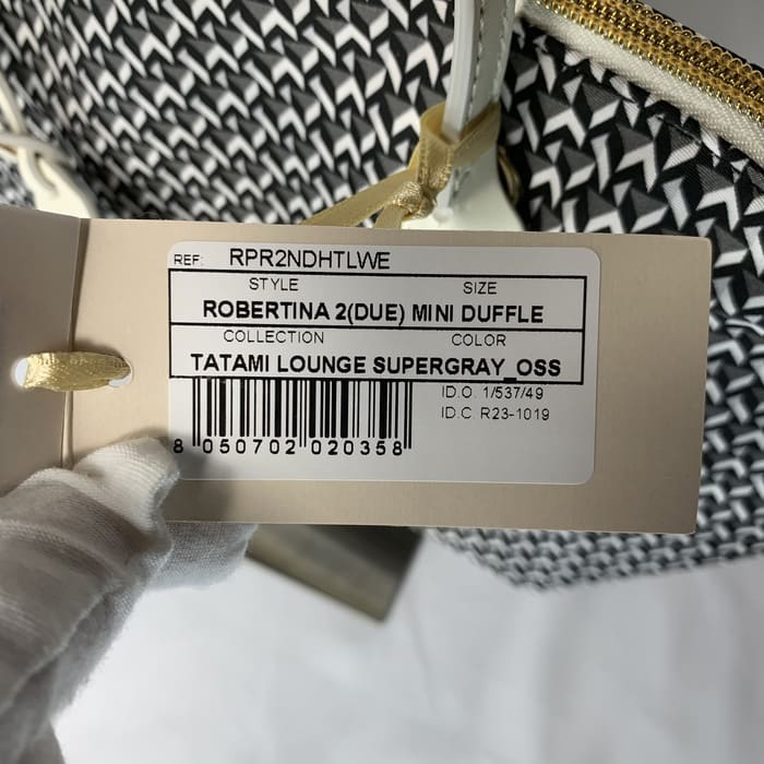 手袋をはめた手がベージュのROBERTA PIERIの商品タグを持ち、スタイル "ROBERTINA 2(DUE) MINI DUFFLE"、カラー "Tatami Lounge Supergray_OSS "など、ミニダッフルバッグのアイテム詳細を誇らしげにイタリア製で表示している。.