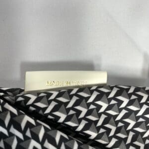 ROBERTA PIERIの黒と白の幾何学模様のミニダッフル生地に、金文字で「MADE IN ITALY」と書かれた白いラベルが貼られている。背景は白無地。.