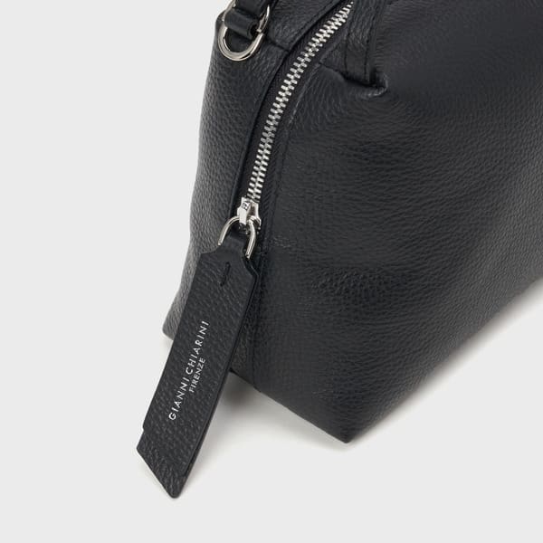 シルバーのファスナー、「GIANNI CHIARINI FIRENZE」と白抜きで書かれた黒のレザータグが付いたGIANNI CHIARINI ALIFA ブラックテクスチャードレザーバッグのクローズアップを、明るい背景で撮影。.