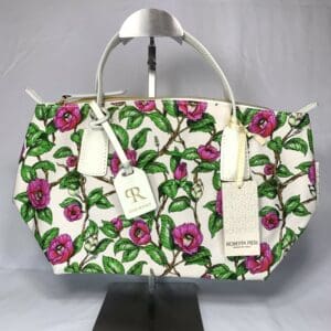 ROBERTA PIERI ミニダッフル ピンクとグリーンの花柄プリント、ゴールドのファスナー、白いハンドルのハンドバッグがメタルスタンドに飾られています。ブランドネームのタグが付いた、スタイリッシュな2WAYバッグです。.