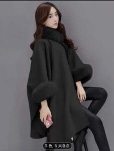 茶色のロングヘアの女性が、襟と袖口にファーがあしらわれたスタイリッシュなブラック・レディースコートを着て、黒いレギンスをはき、ピンクの携帯電話を持っている。無地のグレーを背景にポーズをとっている。.