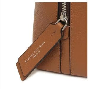 GIANNI CHIARINIのブラウンのレザーバッグのクローズアップ。メタルジッパーと、ホワイトで「GIANNI CHIARINI FIRENZE」と書かれたレザータグが付いています。イタリア製で、時代を超越したイタリアンエレガンスを醸し出しています。.