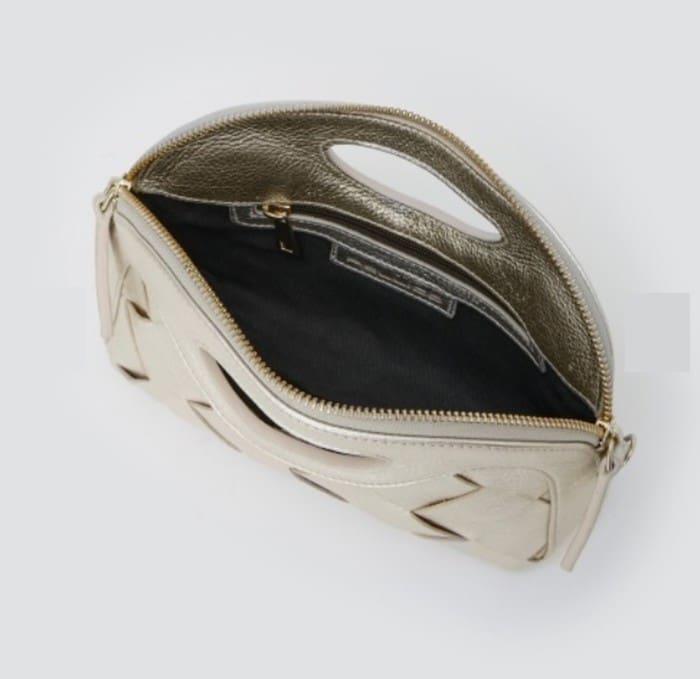 ゴールドのファスナー、ブラックの内装、楕円形のハンドルが付いたベージュのPELICOクラッチバッグを開くと、ライトグレーを背景に内側のコンパートメントが現れる。.