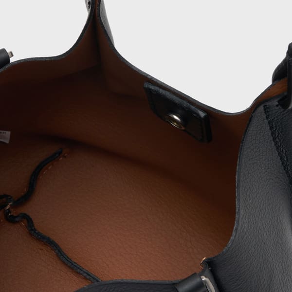 スナップボタン開閉、ドローコード付き。無地を背景に空のバッグを撮影。.