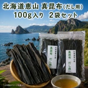北海道恵山の真昆布（だし用）100g入り2袋が、昆布の棒状のものや、澄んで風味豊かなだしスープの入った器とともに並べられています。このシーンは、北海道恵山地域の美しい海岸の風景と山々を背景に、屋外で撮影されています。 この「北海道恵山 真昆布（だし用）100g入り×2袋セット」というプレミアム商品について、日本語で説明されています。.
