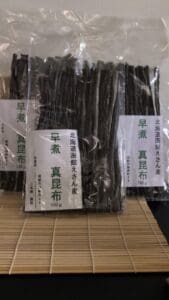無地の背景を背に、竹の敷物の上に、それぞれ100g入りの「北海道恵山 早煮昆布」（3袋セット）が3袋、縦に並べられています。透明なパッケージからは、各袋の中に、濃い色の乾燥昆布がぎっしりと詰められている様子が見えます。.